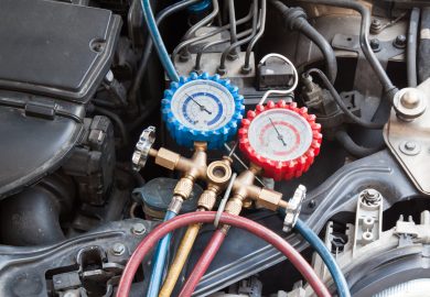 Manometer being used to gauge air conditioning pressure in auto vehicle.